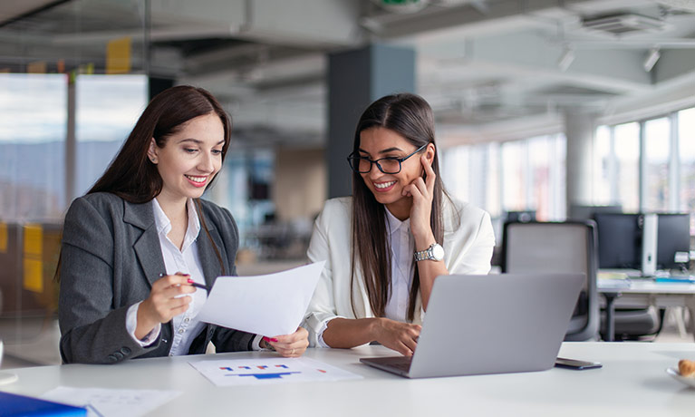 Two women sat at a desk looking over some documents together.