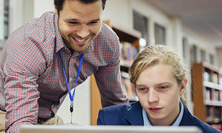 teacher helping a student at a computer in a library.