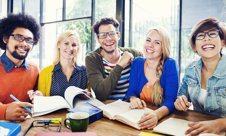 A group of people smiling at the camera with books and papers in front of them.