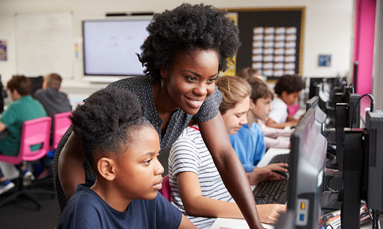 Lecturer helping a student at a computer screen in a classroom with other students