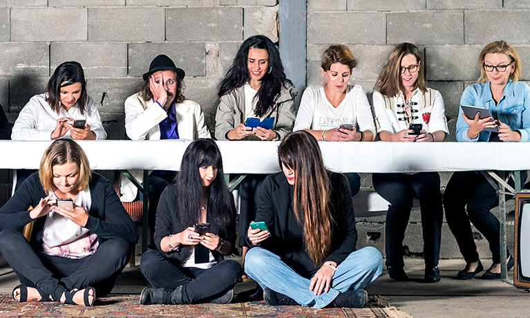 Nine students around a table looking at there electronic phones and tablet devices