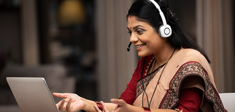 Asian woman sitting at a table with headset talking into a laptop computer